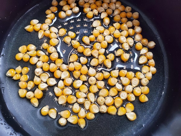 片手鍋を傾けてポップコーン豆とサラダ油と塩を、鍋の中でなじませている画像です。